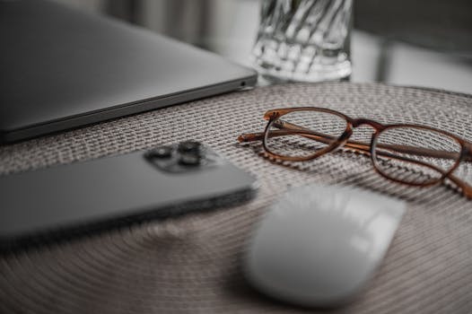 Close-up of a workspace featuring gadgets, eyeglasses, and a mouse in a minimalist setting.