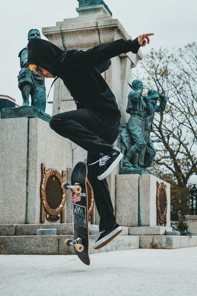 Man In Black Pants And Hoodie Jacket Doing A Kick Flip On Skateboard