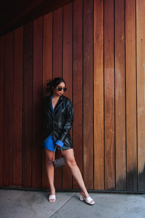Woman in Black Leather Jacket Standing Beside a Wooden Wall