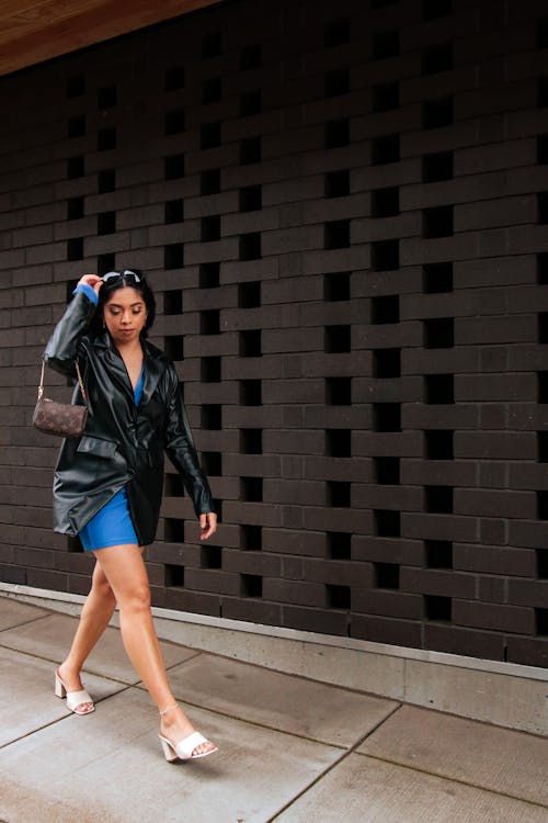 Woman in Black Leather Blazer Walking on the Sidewalk while Looking Afar