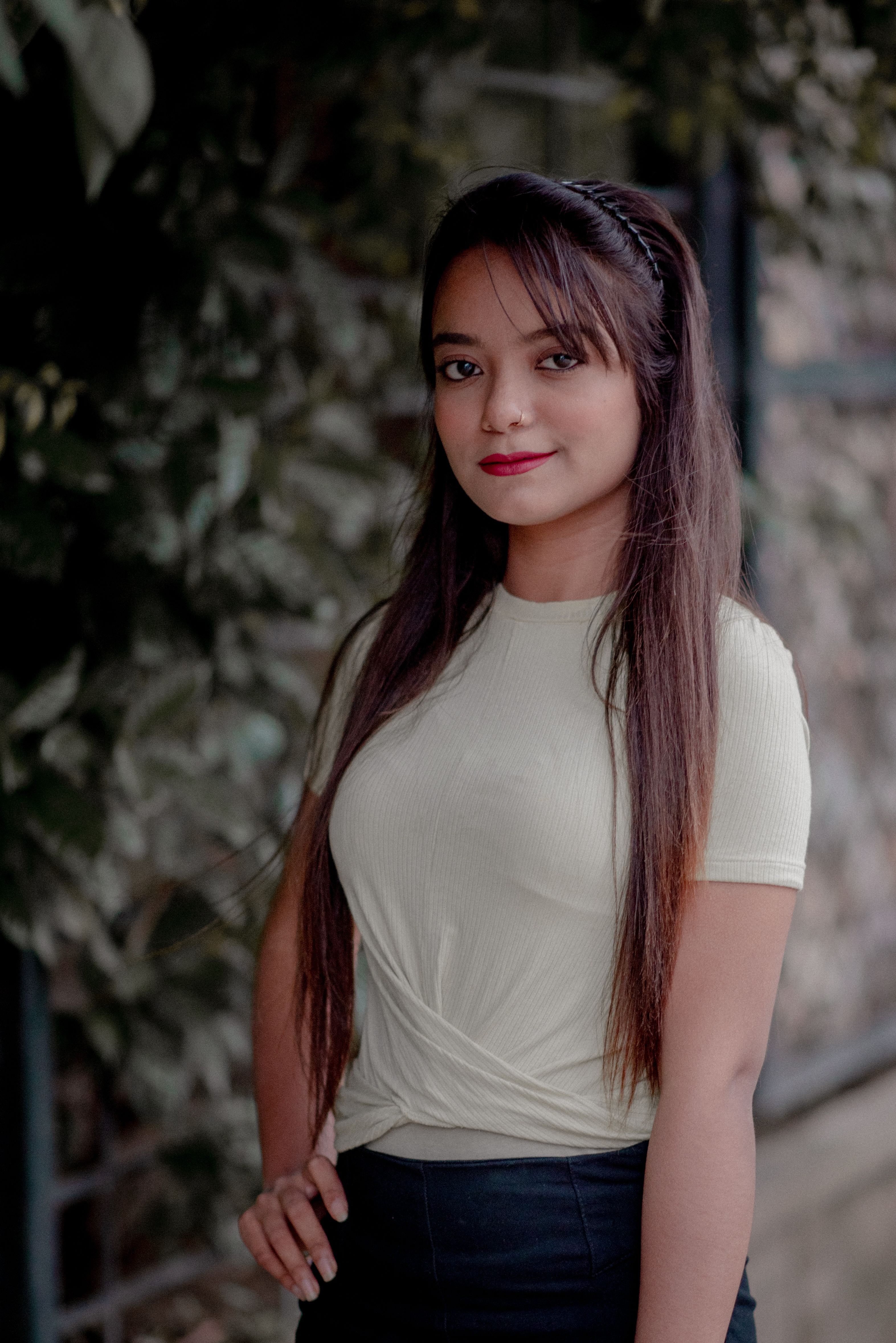 Portrait of a young woman with long hair and red lips standing outdoors with hand on waist.
