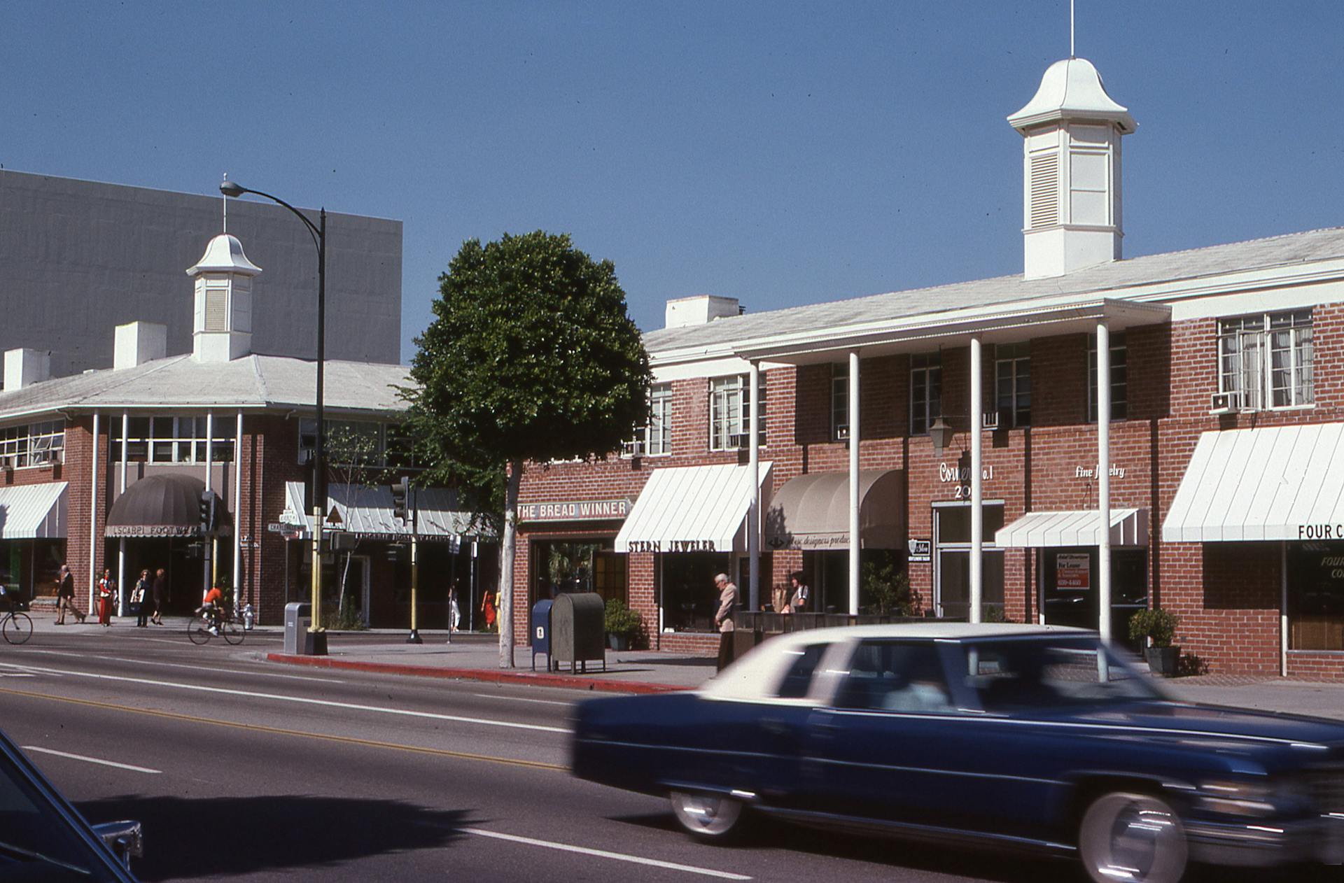 A busy street scene featuring classic cars and charming brick storefronts under a clear sky.