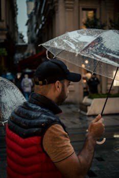 A man with an umbrella walks through a rainy city street, showcasing urban life under wet weather.