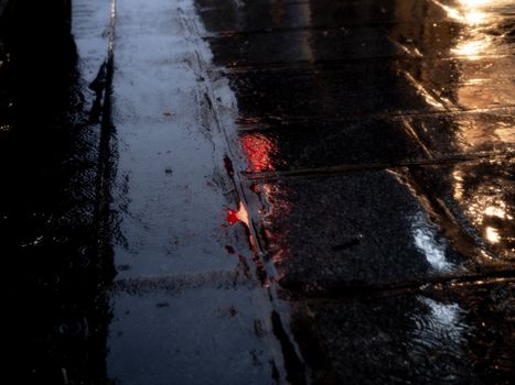 A dark, moody night shot of a wet urban sidewalk reflecting city lights after rain.