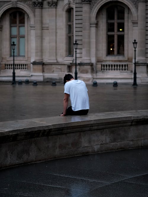 Man in White Shirt Sitting on a Concrete Barrier