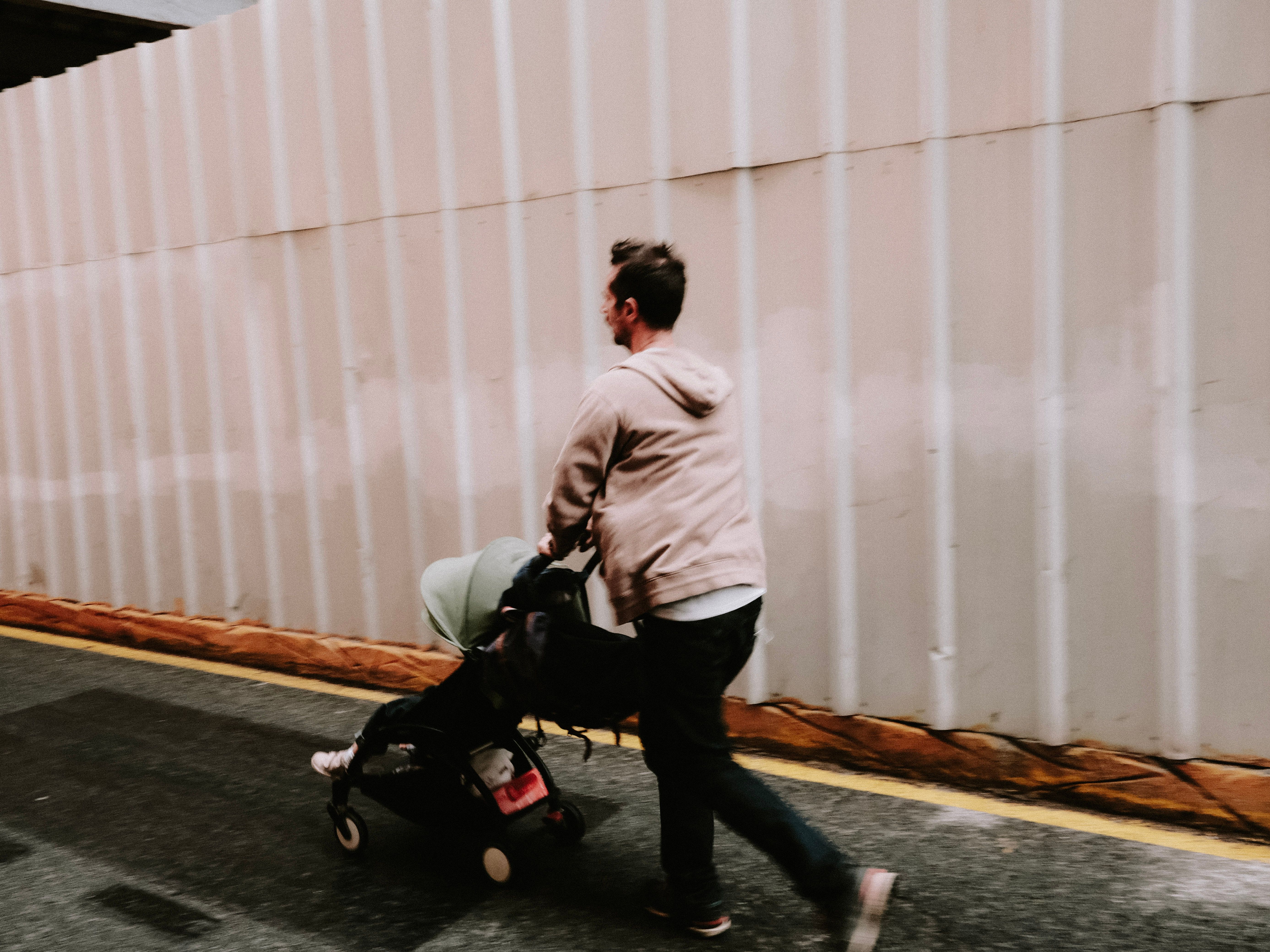 A man pushing a stroller down a street alongside a corrugated wall, captured in an urban setting.