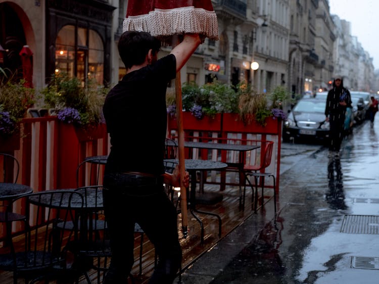 Man Setting Up Umbrella Over Restaurant Tables On Street