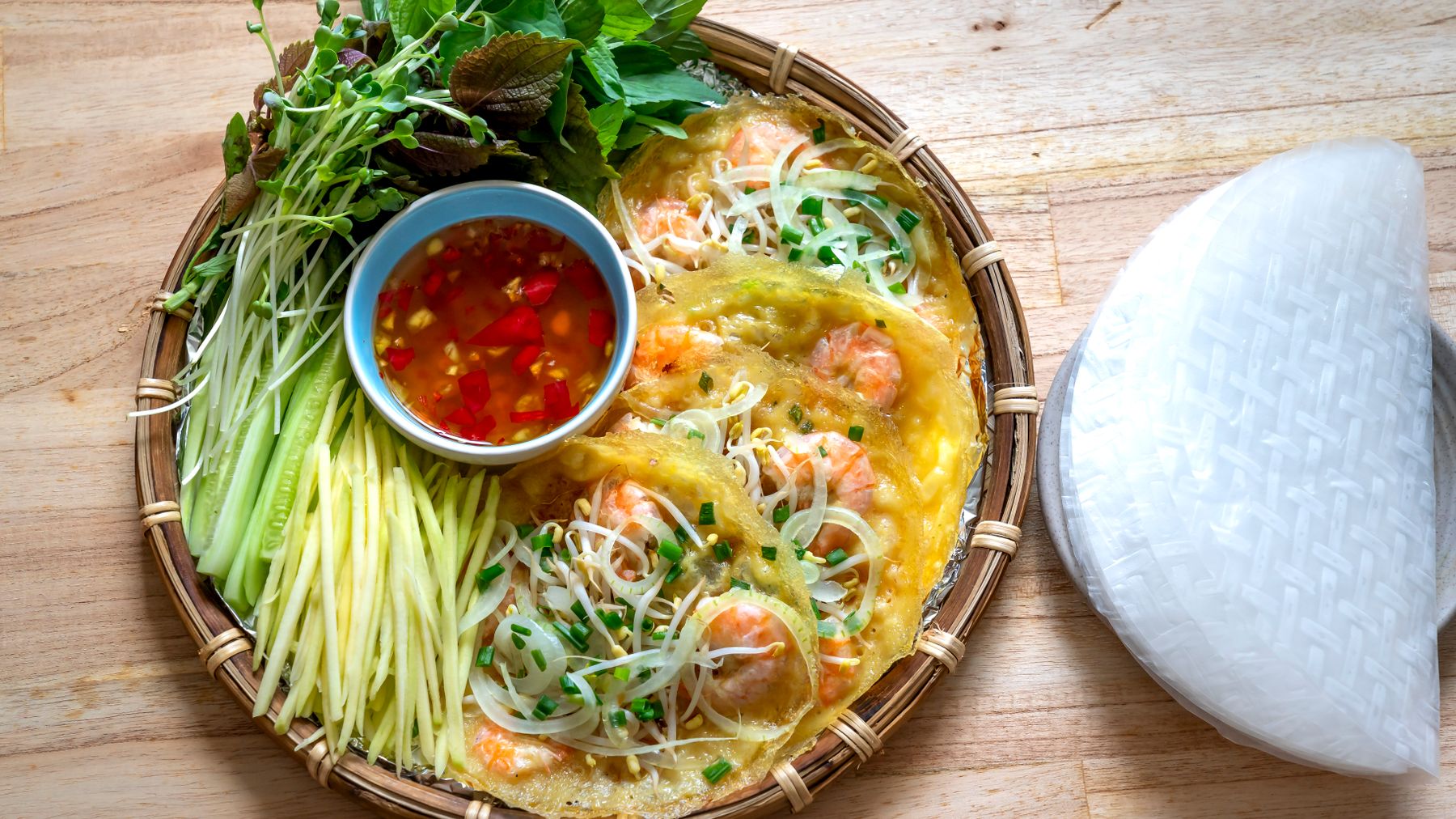 Draufsicht auf lebhaftes vietnamesisches Banh Xeo mit frischen Kräutern und einer Beilage aus Chilisauce.