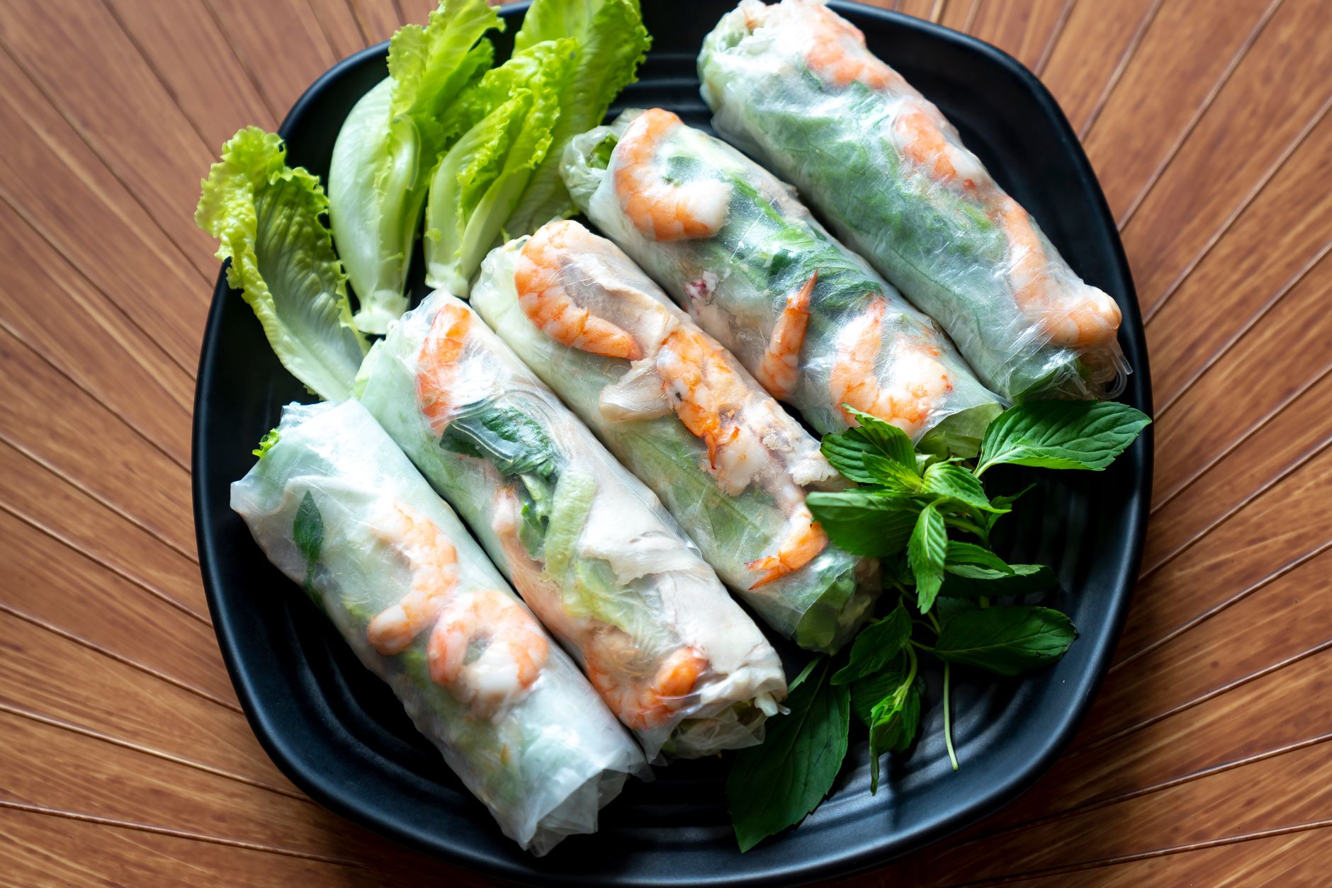 Delicious Vietnamese spring rolls with vegetables and shrimp served on a black plate.