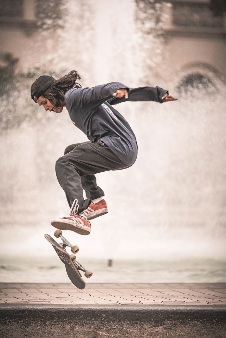 Energetic skateboarder performing a mid-air trick in front of a fountain.. energetic, skateboarder, performing