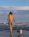 Topless Woman in Black and White Striped Shorts Standing on Beach Shore