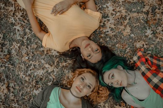 A top view of three women lying on a leafy ground, capturing the essence of friendship in the fall.