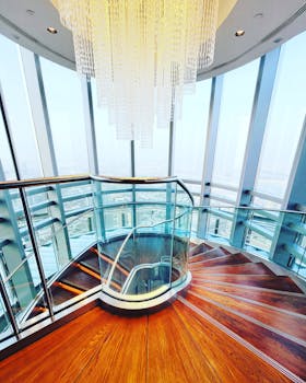 Elegant staircase with crystal chandelier in a modern glass building interior.
