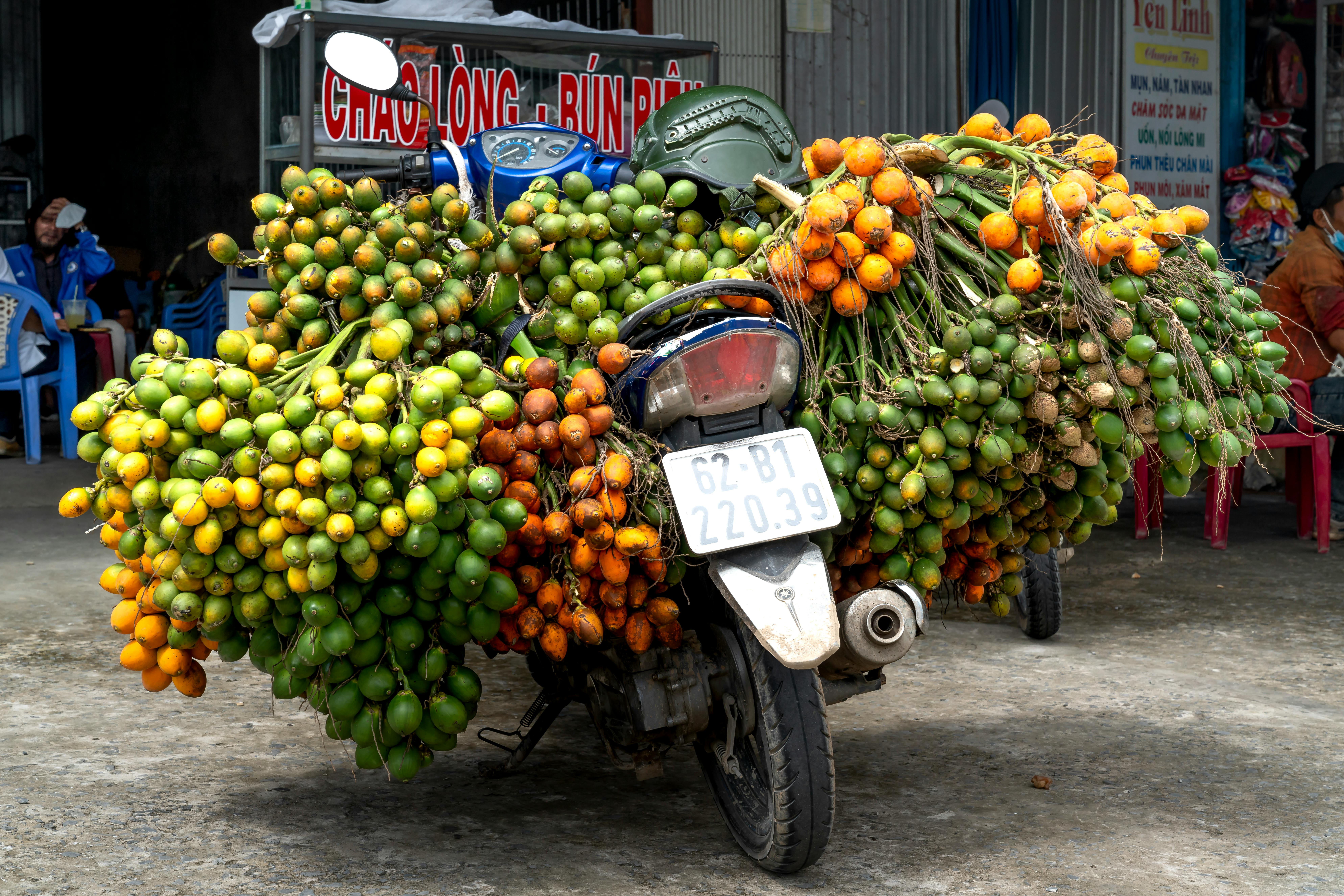 Motorcycle overloaded with fresh, colorful betel nuts, parked in a lively market scene.