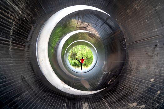 A person performs a yoga pose in a dramatic setting inside a large metal tunnel.