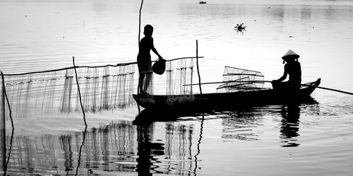 Free Black and white silhouette of fishermen in a canoe on a tranquil river with fishing nets. Stock Photo