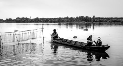 Free Black and white image capturing fishermen in a boat setting nets on a calm lake. Stock Photo