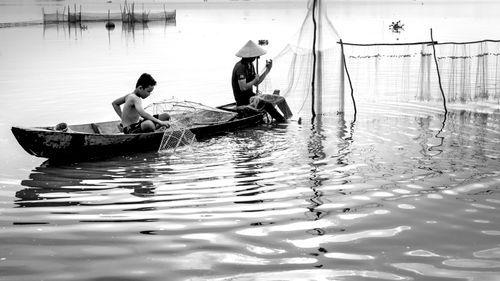 Free Black and white photo of fishermen on a lake, using nets to catch fish in a traditional boat. Stock Photo