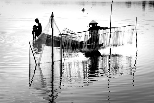 Free Black and white photo of fishermen with nets on a boat casting nets in a calm river. Stock Photo