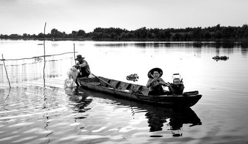 Free Black and white image of fishermen in a wooden boat on a calm lake, highlighting traditional fishing methods. Stock Photo