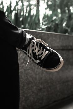 Fashionable black sports shoe with laces resting on a stone ledge outdoors.