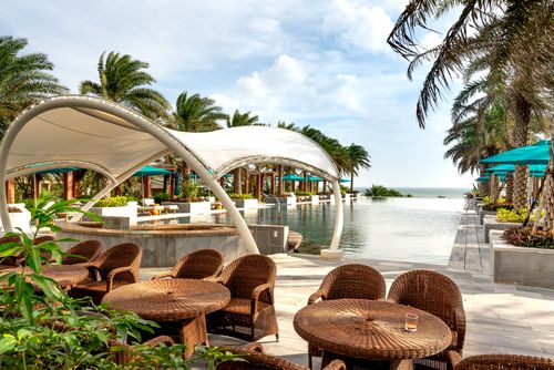 Free Luxurious tropical resort poolside with palm trees, wicker chairs, and ocean view. Stock Photo