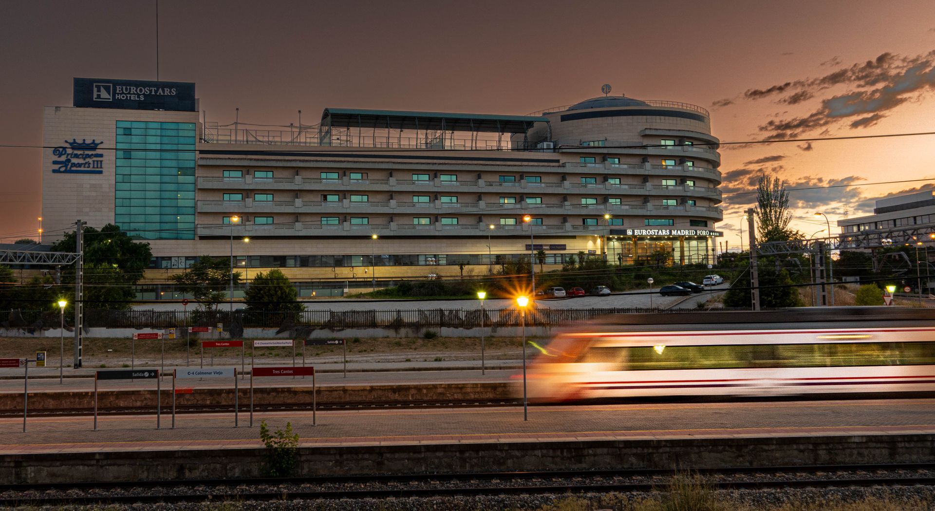 A high-speed train passes Eurostars Hotel in Madrid, captured in motion blur at dusk.