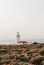 White and Red Lighthouse on Green Grass Field Under White Sky