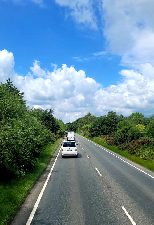 Free A picturesque road trip view with clear blue sky and lush greenery on a sunny day. Stock Photo