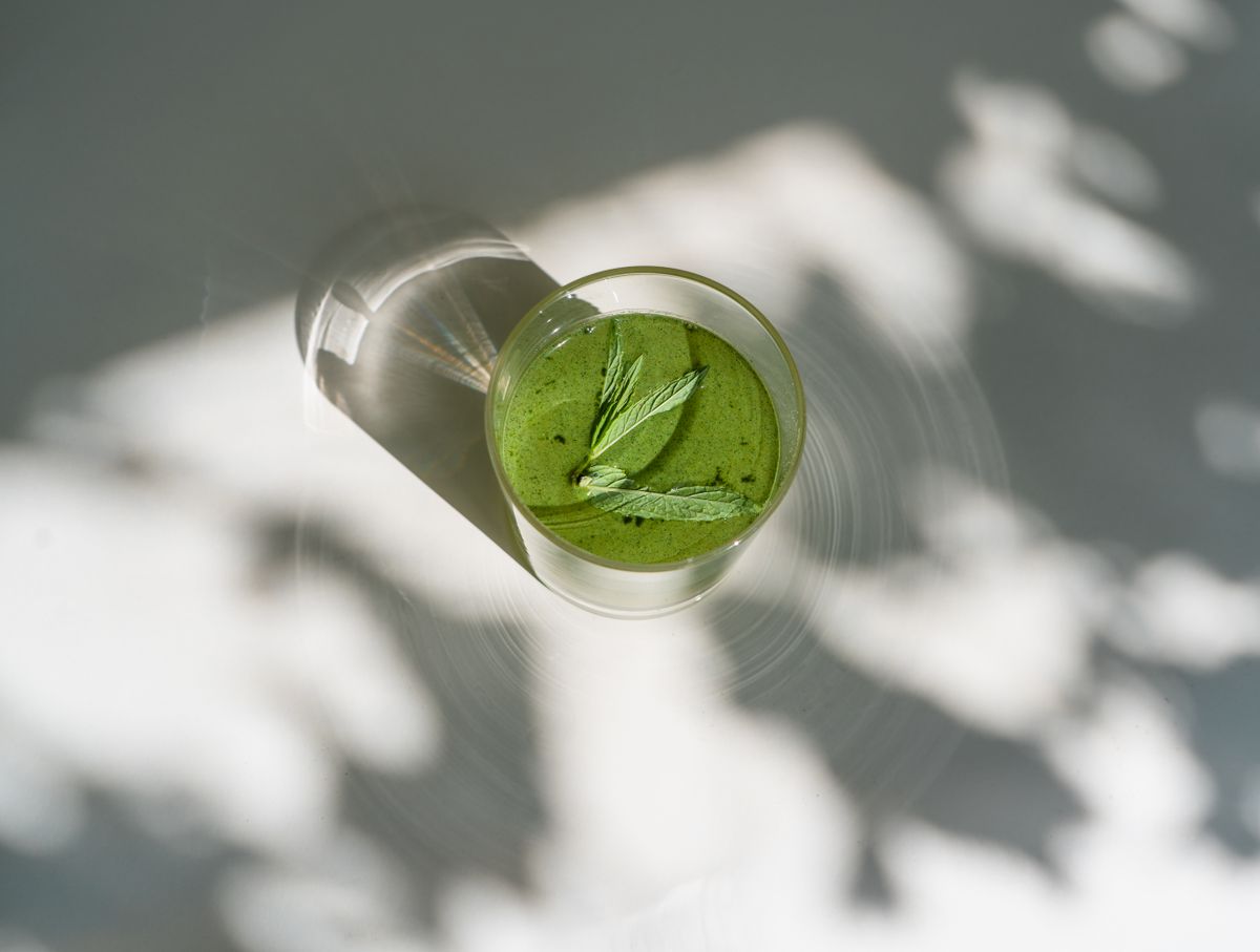 Matcha smoothie recipe in a clear glass with a smooth green surface and mint leaves