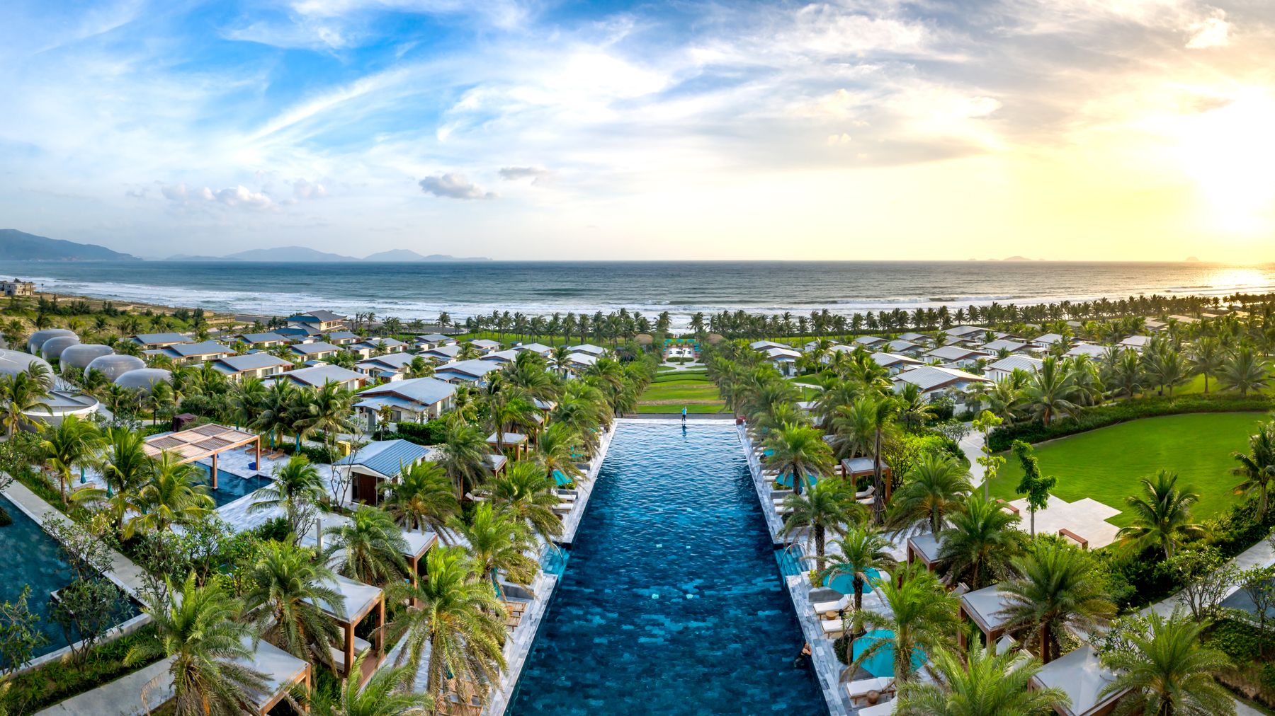 Discover a stunning beach resort with lush gardens and infinity pool overlooking the ocean at sunset.