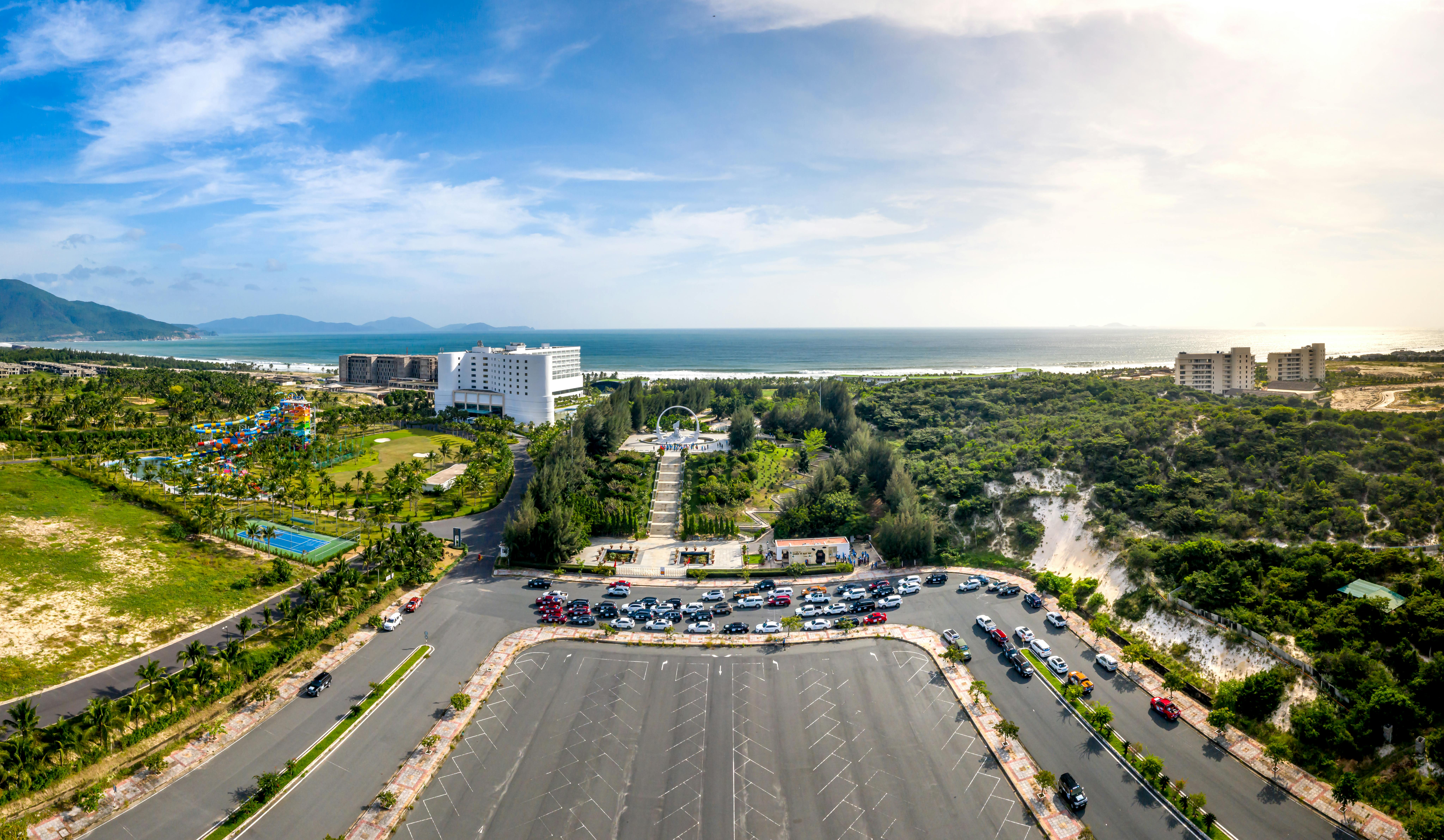 A stunning aerial view of a coastal resort featuring lush greenery, a parking lot, and the ocean beyond.