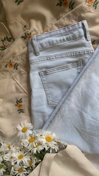 Fashion flat lay with floral patterns, denim jeans, daisies, and tote bag.