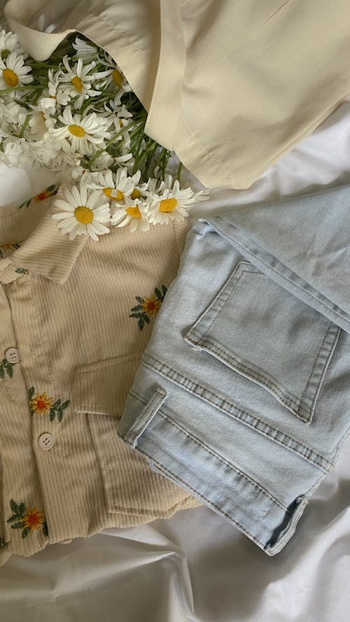Blue Denim Jeans Beside Daisy Flowers on White Fabric
