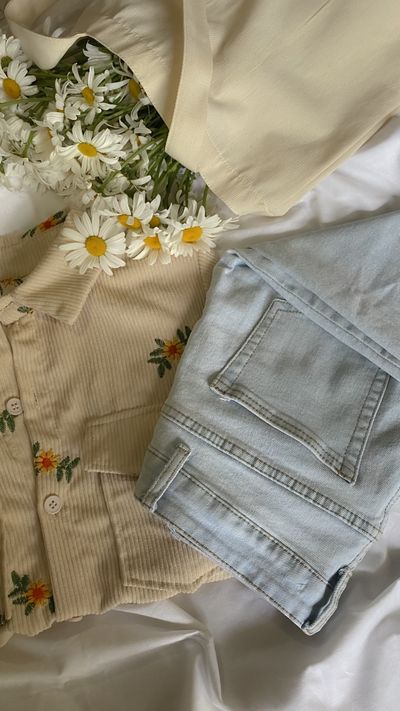 Embroidered cream shirt folded beside pale washed jeans and daisies, photo by Karina Kholina on Pexels