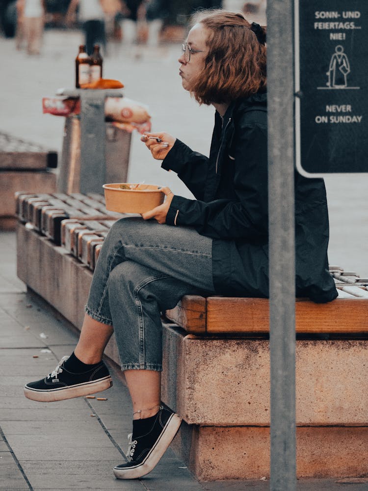 Woman Wearing Eyeglasses Sitting On The Bench Eating