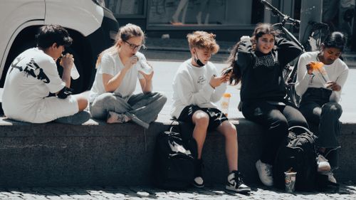 Free Group of teenagers sitting on a ledge, enjoying drinks and socializing outdoors on a sunny day. Stock Photo