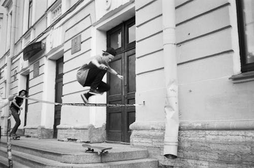 Grayscale Photography of Man Riding Skateboard Making Tricks Near Concrete Building