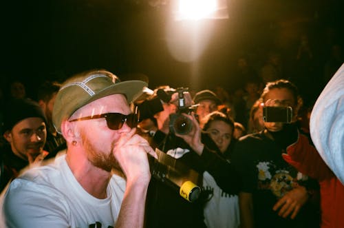 Man Speaking on Microphone Surrounded by People Taking Photo