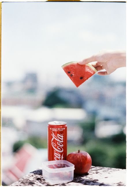 A Coca-Cola can with watermelon and apple outdoors, evoking a refreshing summer vibe.