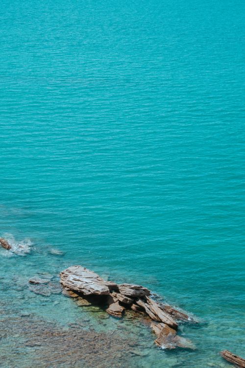 Free Serene aerial view of turquoise ocean and rocky shoreline, perfect for calm and nature themes. Stock Photo