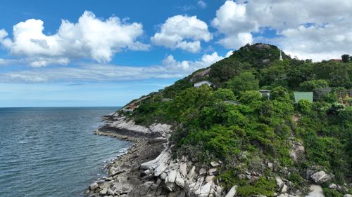Free Breathtaking coastal landscape with vibrant greenery, rocky shore, and a clear blue sky with fluffy clouds. Stock Photo