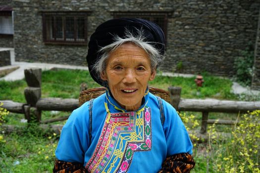 Portrait of a smiling elderly Tibetan woman in traditional attire outdoors in Tibet.