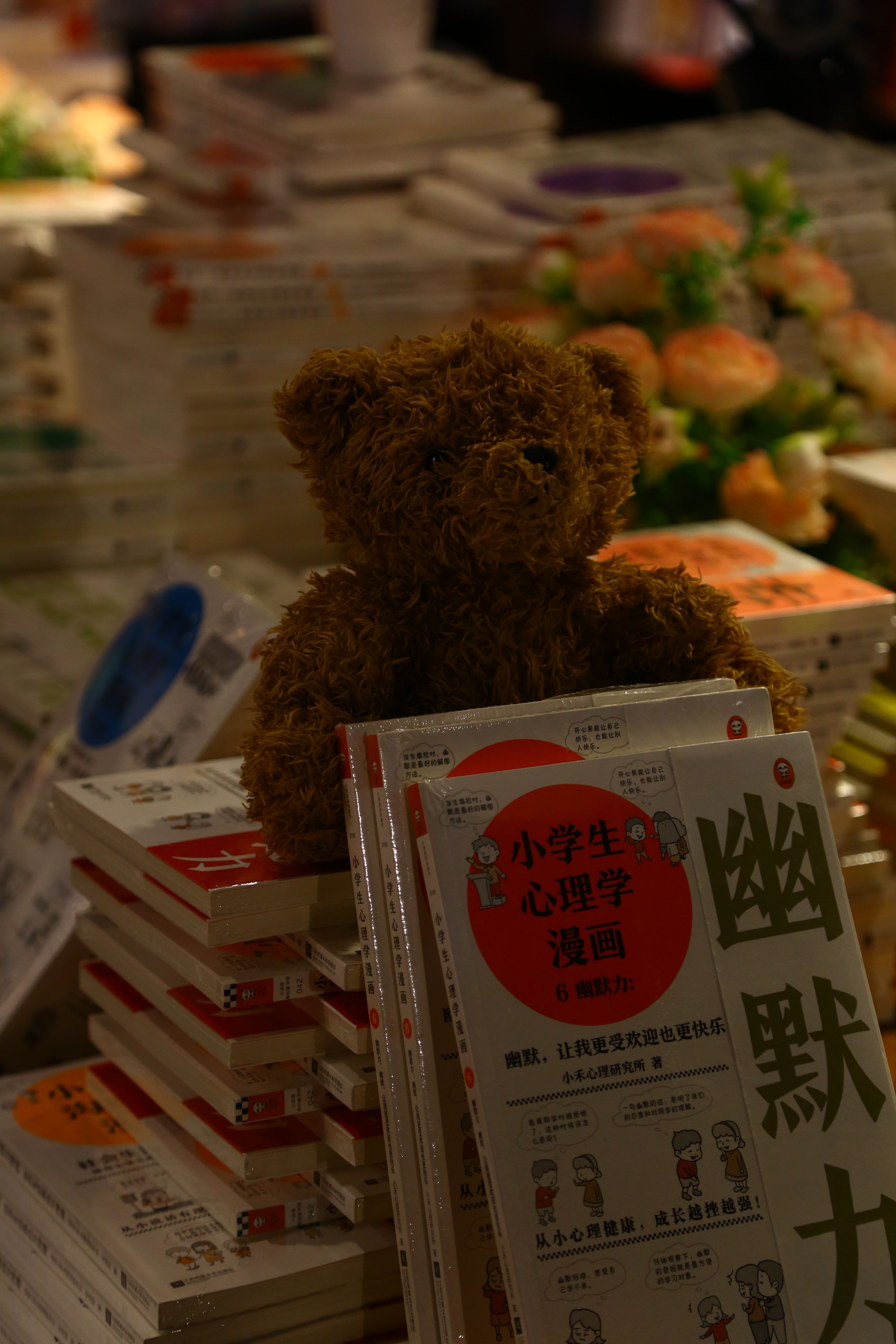 A plush teddy bear sits among stacks of books in a warm, inviting setting.
