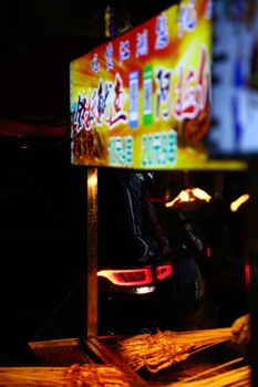 Vibrant night scene of a food stall with an illuminated sign and car taillights.