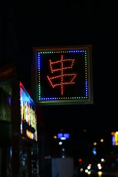 Bright neon sign with Asian character illuminating a street food stall at night.