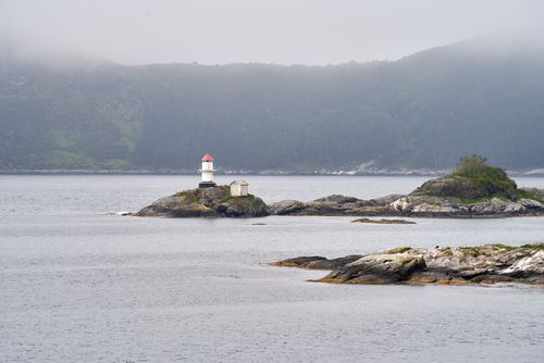 Free A lighthouse on a rocky island amidst the misty sea and mountains under overcast skies. Stock Photo