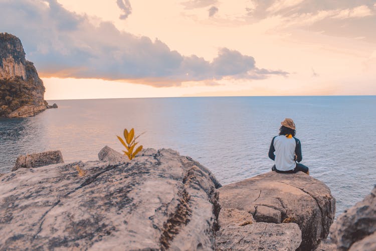 Person Sitting On Cliff Near Body Of Water