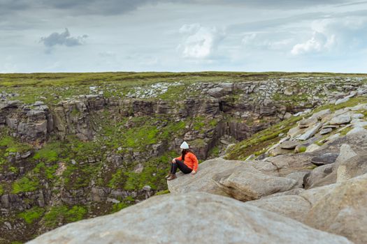 Man in Red Jacket and Black Pants Sitting on Rock Mountain