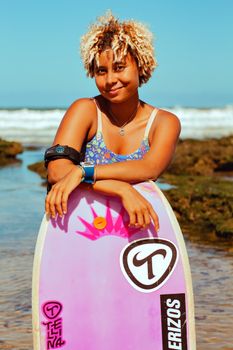 Bright and cheerful young woman with surfboard on a sunny coast, ready for surfing.